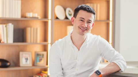 Smiling man in white shirt posing against wooden shelving unit in bright interior